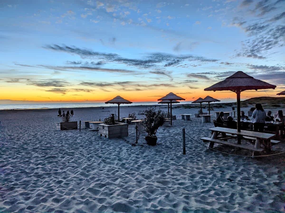 Strandbar in Hargen aan Zee bei Sonnenuntergang mit Holztischen, Bastschirmen und Blick auf die Nordsee. Strandbar in Hargen aan Zee bei Sonnenuntergang mit Holztischen, Bastschirmen und Blick auf die Nordsee.