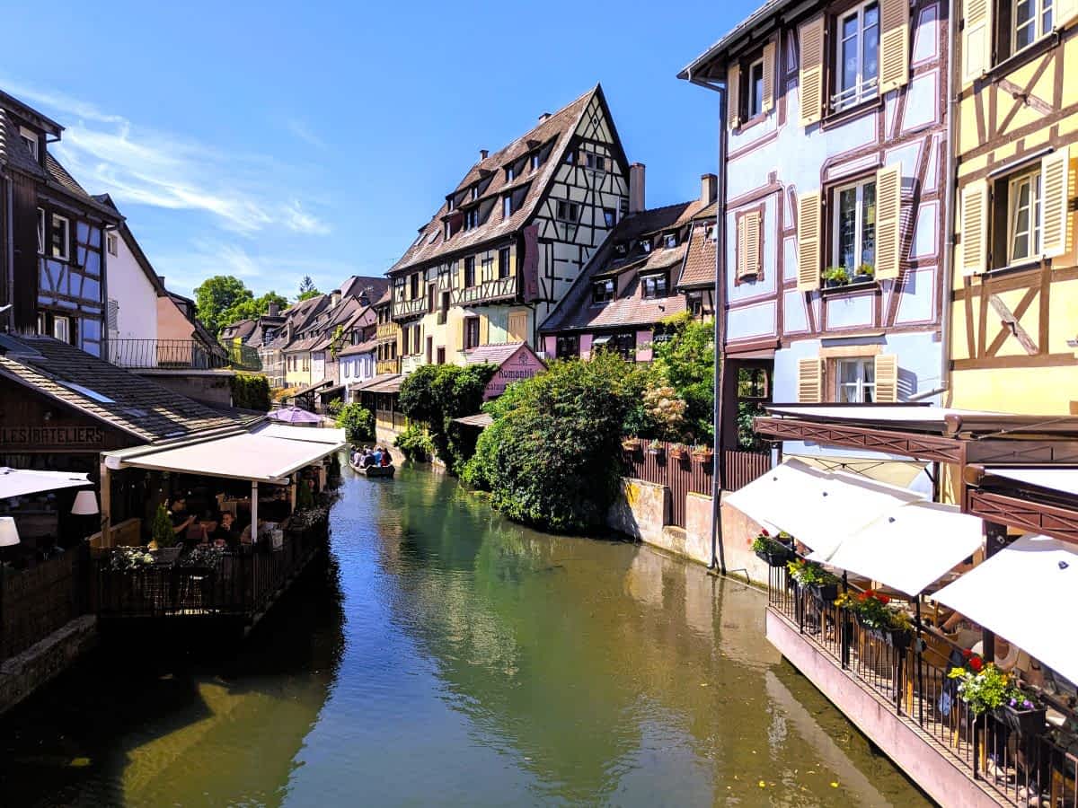 Malerischer Blick auf den Kanal in "Petite Venise" (Klein-Venedig) in Colmar, gesäumt von bunten Fachwerkhäusern und Restaurants mit Sonnenschirmen.