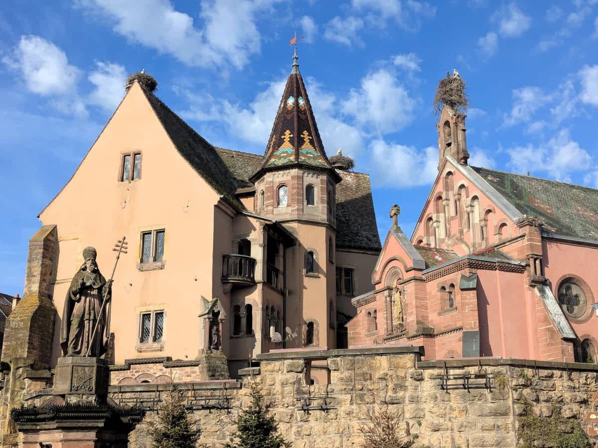 Die Kapelle von Eguisheim und die Burgmauer mit mehreren Storchennestern auf den Giebeln und Türmen.